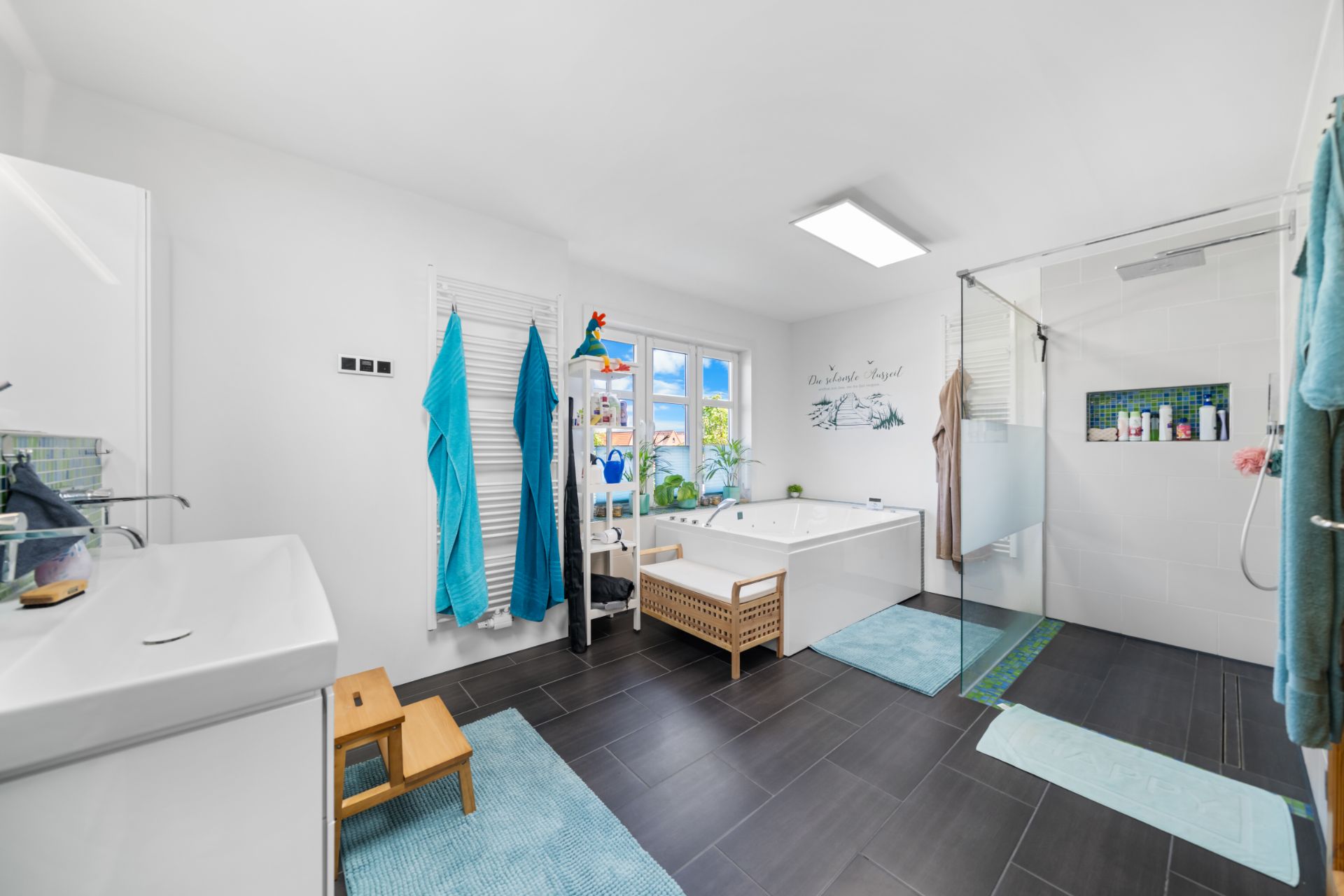 Helles Badezimmer mit Dusche, Badewanne, Waschbecken und Handtüchern, großes Fenster im Hintergrund.