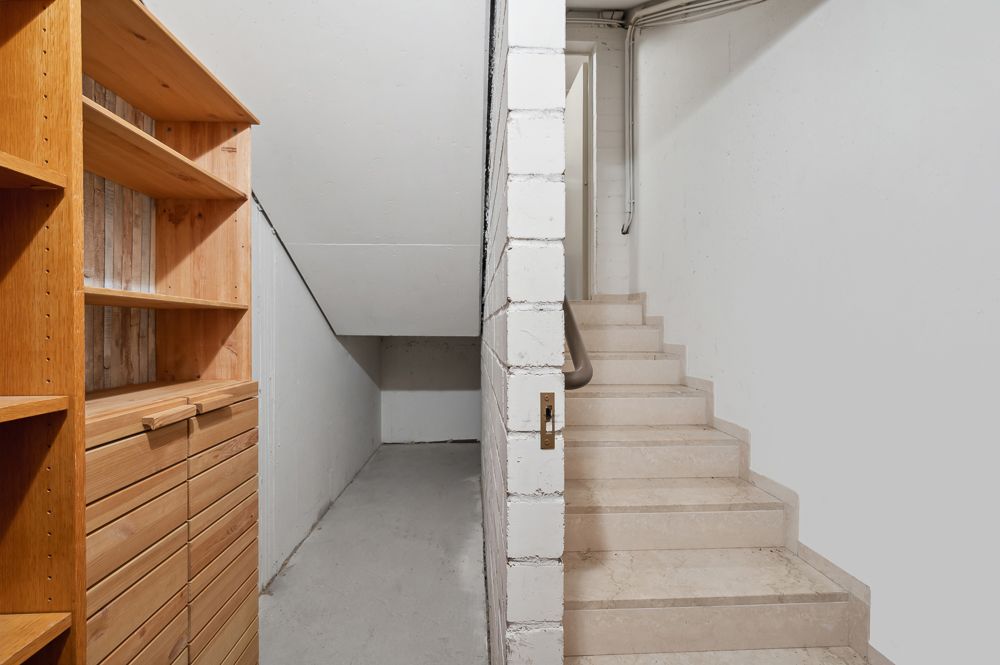 Keller mit Holzregal und Treppe, geteilt durch eine weiße Wand.