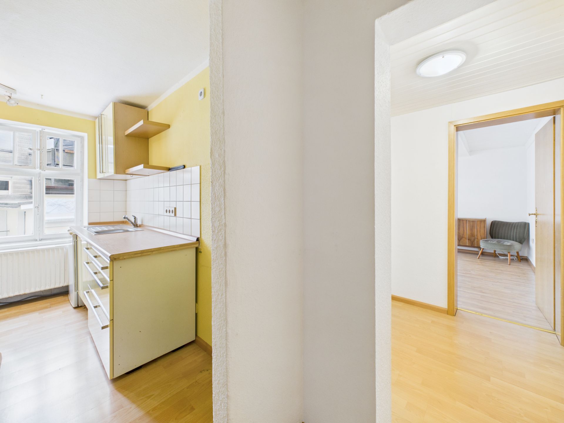 Helle Küche mit gelber Wand und angrenzendem Wohnzimmer mit Holzfußboden.