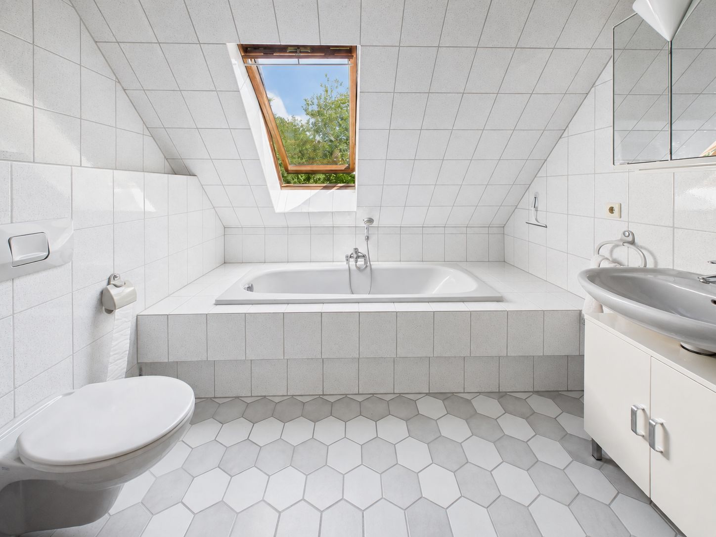Helles Badezimmer mit Badewanne unter Dachfenster, Toilette und Waschbecken.