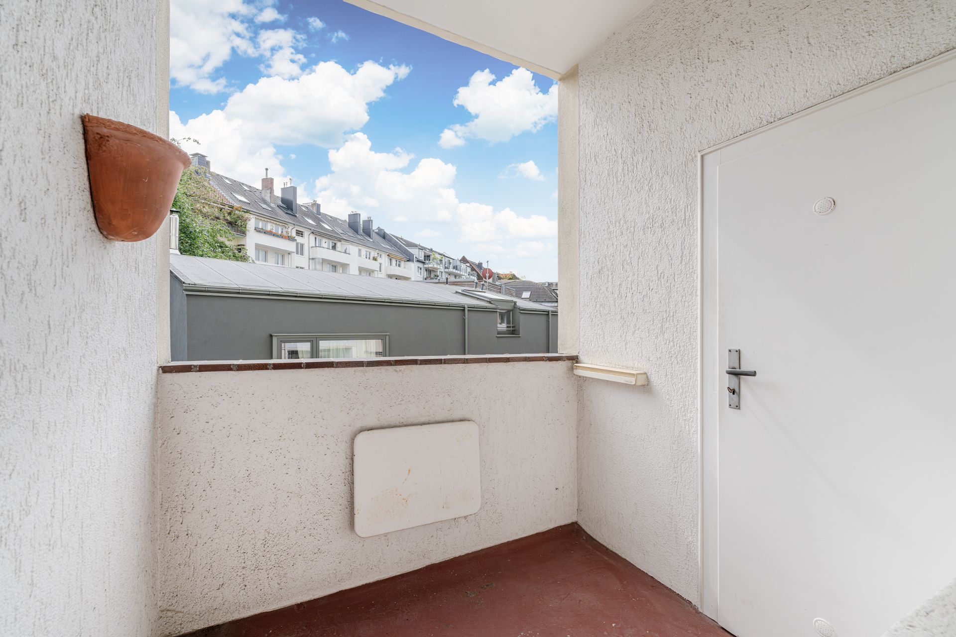Kleiner Balkon mit weißer Tür und Blick auf Wohnhäuser unter blauem Himmel.