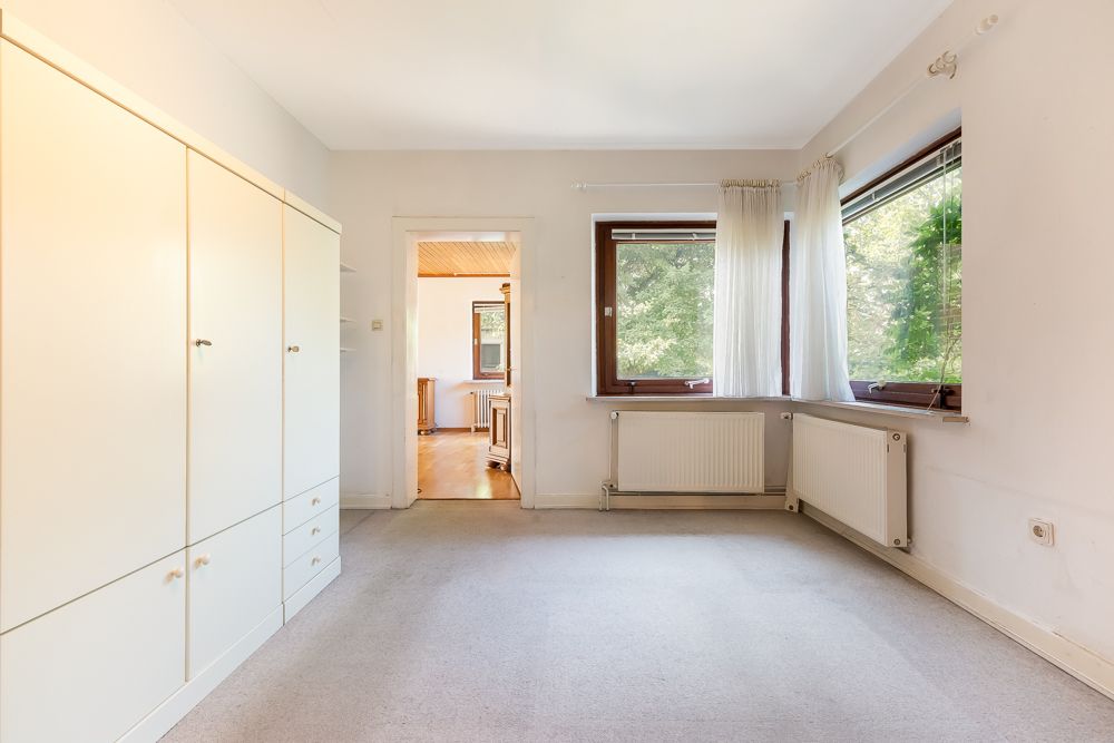 Helles Zimmer mit großem weißen Kleiderschrank, Teppichboden und zwei Fenstern mit weißen Vorhängen.