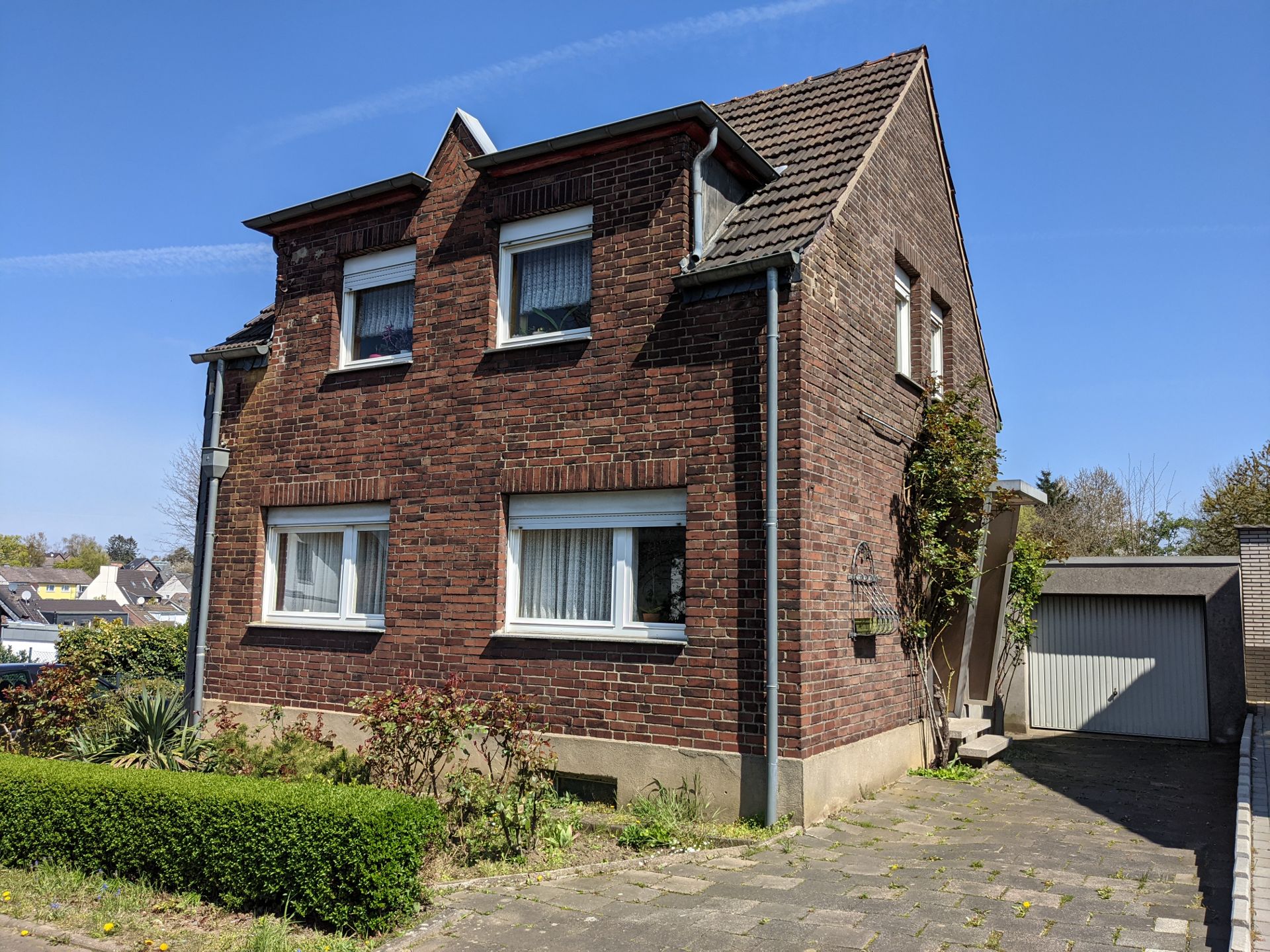 Backsteinhaus mit Satteldach, Vorgarten und angrenzender Garage an einem sonnigen Tag.