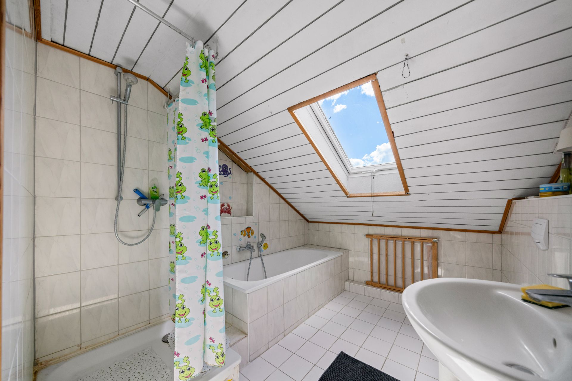 Badezimmer mit Dusche, Wanne, Waschbecken und Dachfenster unter schräger Decke.