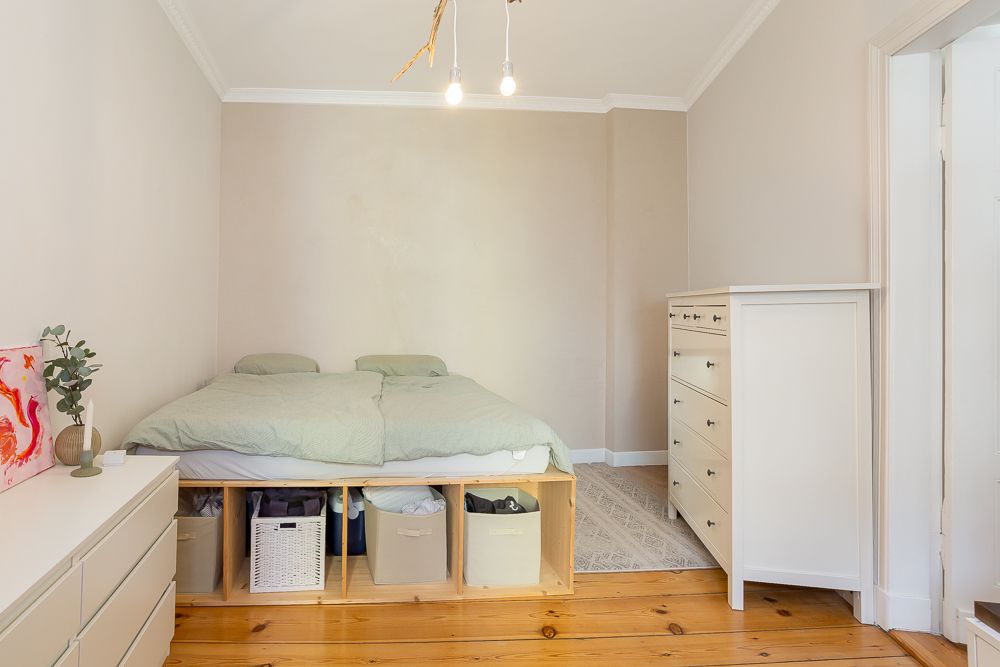 Schlafzimmer mit Bett, Kommoden und Aufbewahrungsboxen unter dem Bett auf Holzboden.