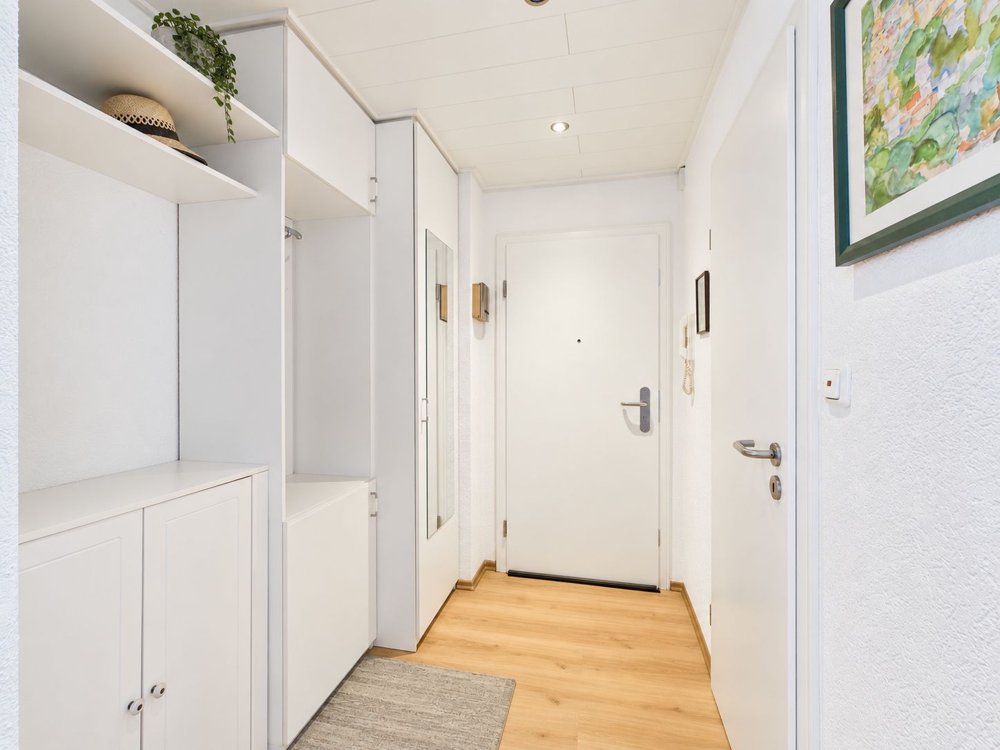 Heller Flur mit weißer Tür, Garderobe, Holzboden, Teppich und Bild an der Wand.
