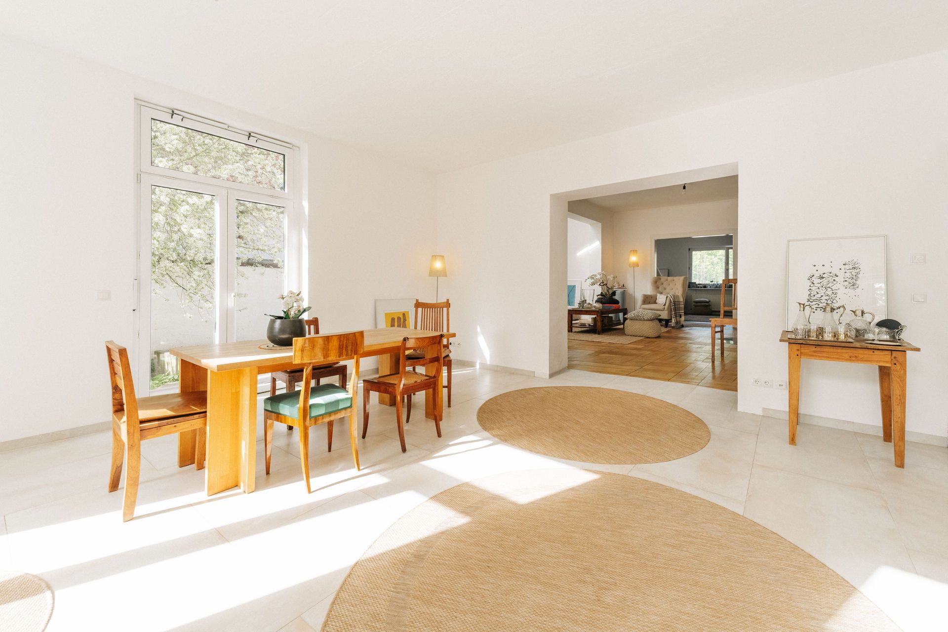 Heller Essbereich mit Holztisch, Stühlen und runden Teppichen, Zugang zum Wohnzimmer.