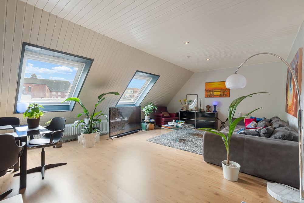 Helles Wohnzimmer mit Dachschrägen, großen Fenstern, Pflanzen, Sofa und Esstisch.