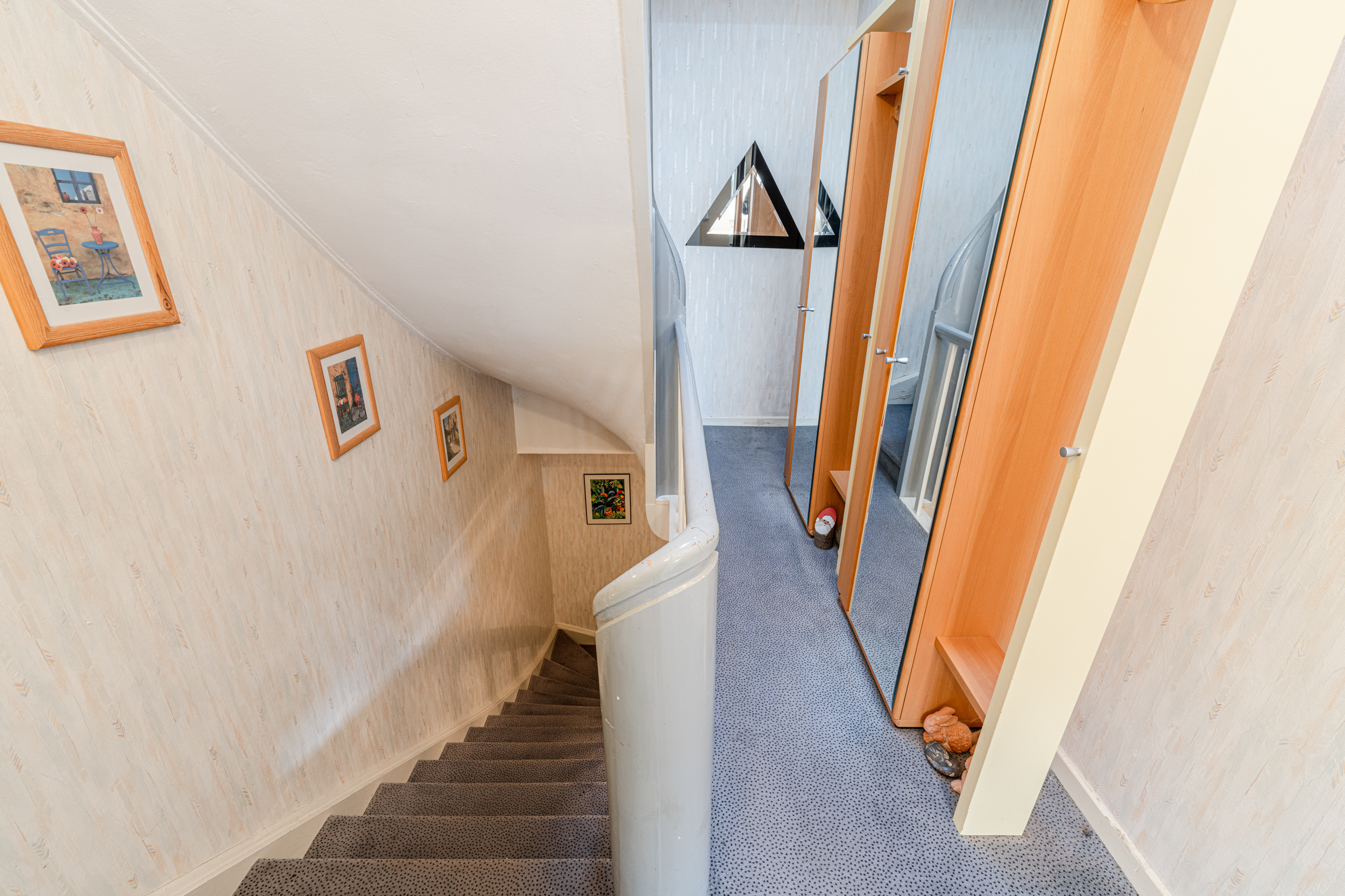 Treppenaufgang mit gerahmten Bildern an der Wand und Spiegelschrank auf dem Flur.