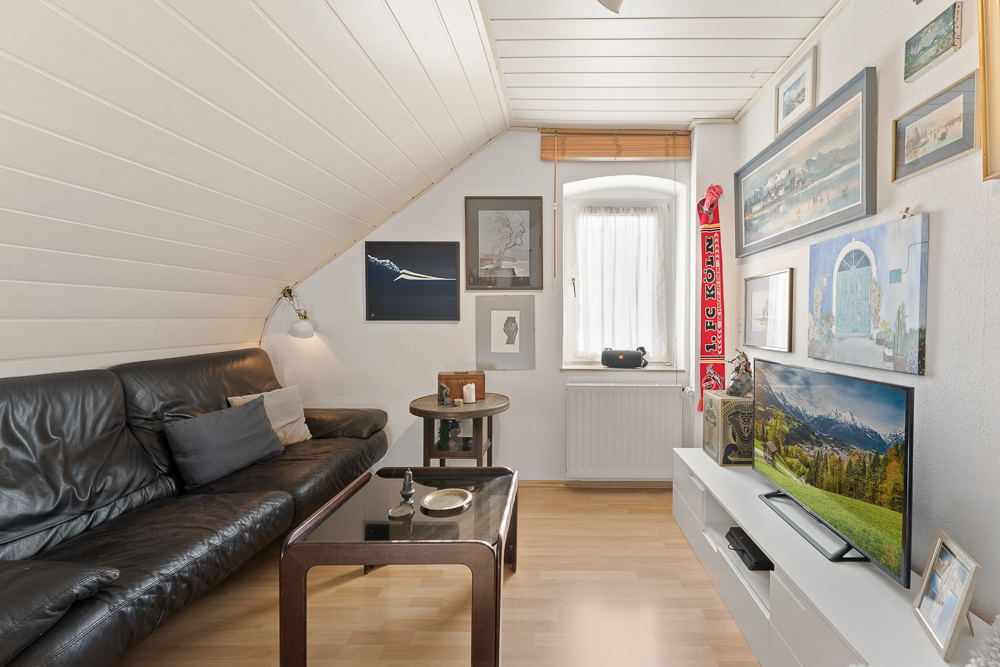 Wohnzimmer mit schwarzem Ledersofa, Couchtisch, Fernseher und Bildern an der Wand.