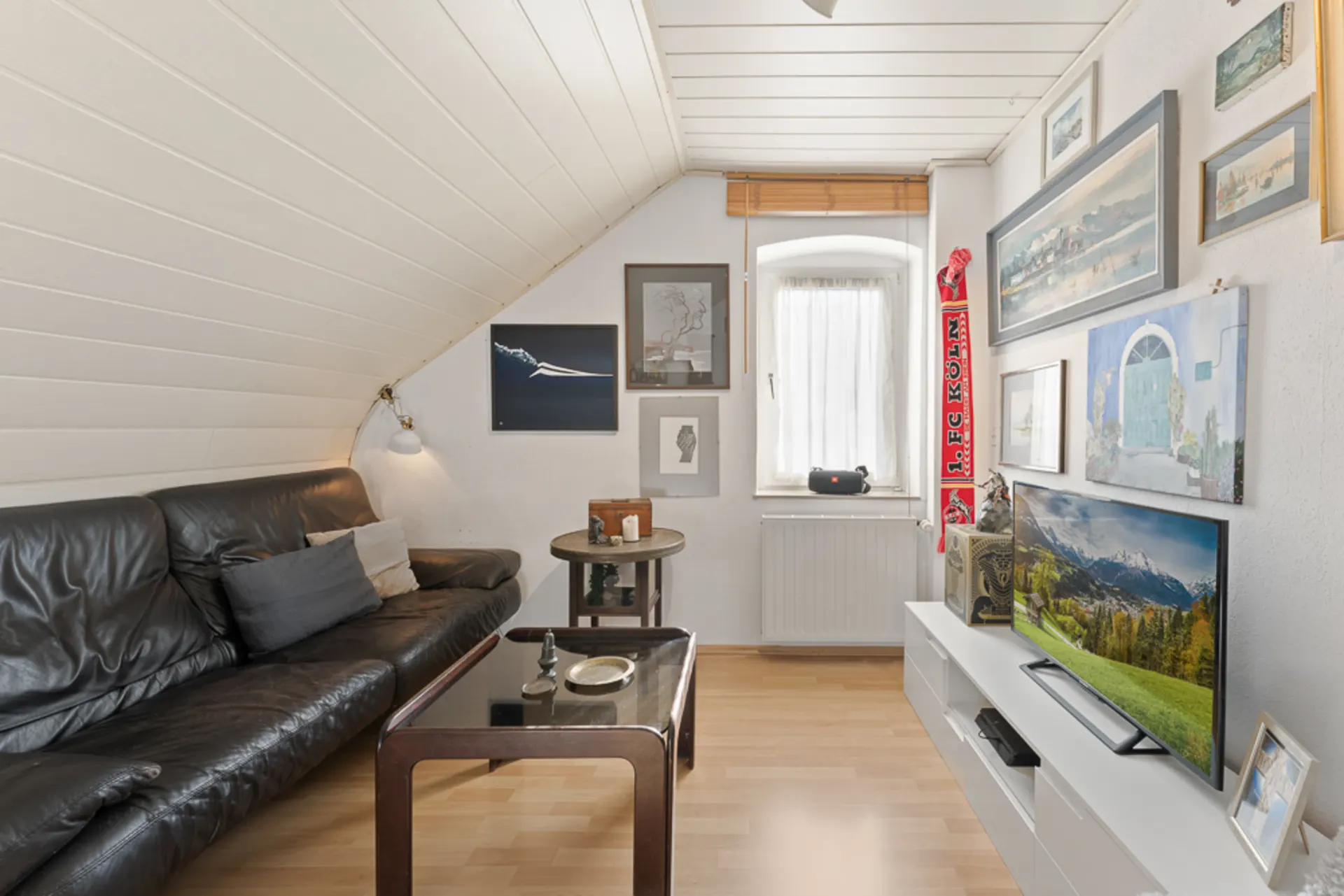 Wohnzimmer mit schwarzem Ledersofa, Couchtisch, Fernseher und Bildern an der Wand.
