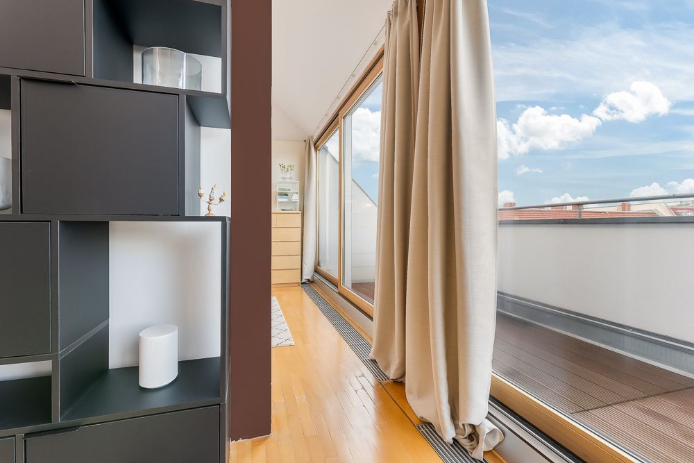 Helle Wohnung mit Holzfußboden, Vorhang und Zugang zu einer Terrasse mit Glasbrüstung.