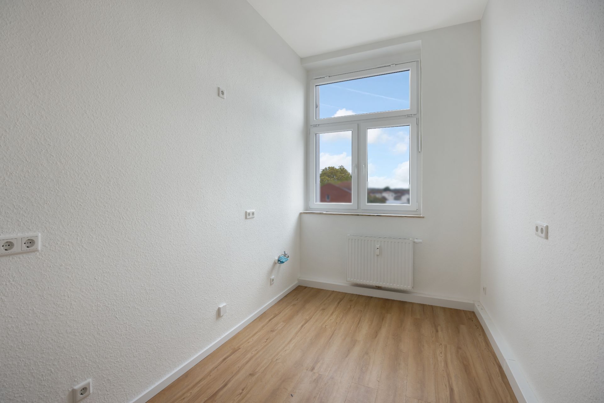 Kleiner, leerer Raum mit weißer Wand, Holzfußboden und Fenster mit Blick nach draußen.