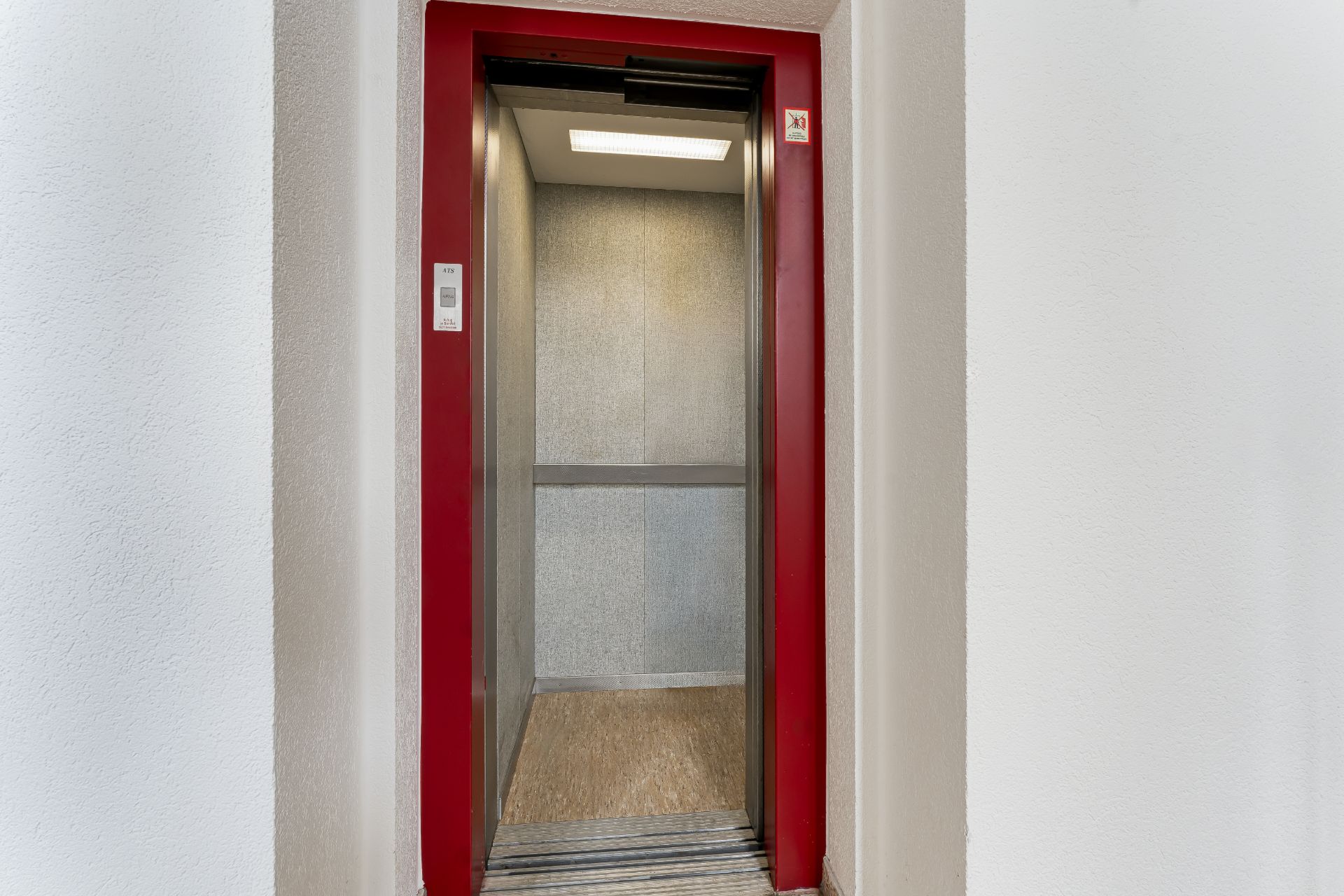 Offene Aufzugtür mit rotem Rahmen in einem Wohnhaus, Innenraum beleuchtet.