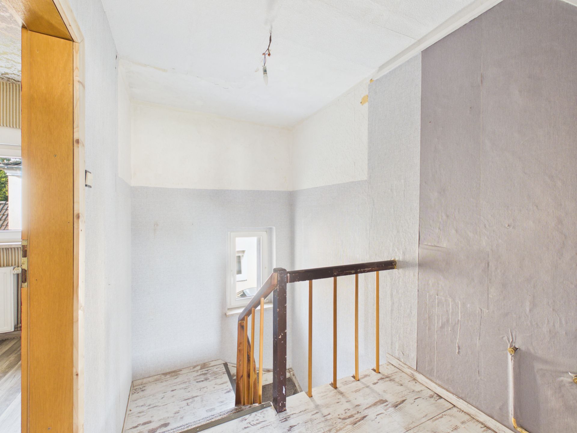 Heller Treppenabsatz mit Holzgeländer und kleinem Fenster an der Wand.
