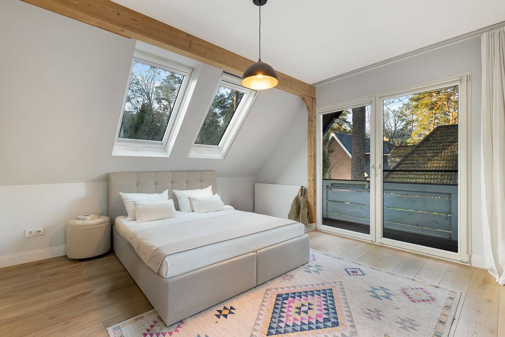 Helles Schlafzimmer mit Doppelbett, Dachfenstern und Balkonzugang.