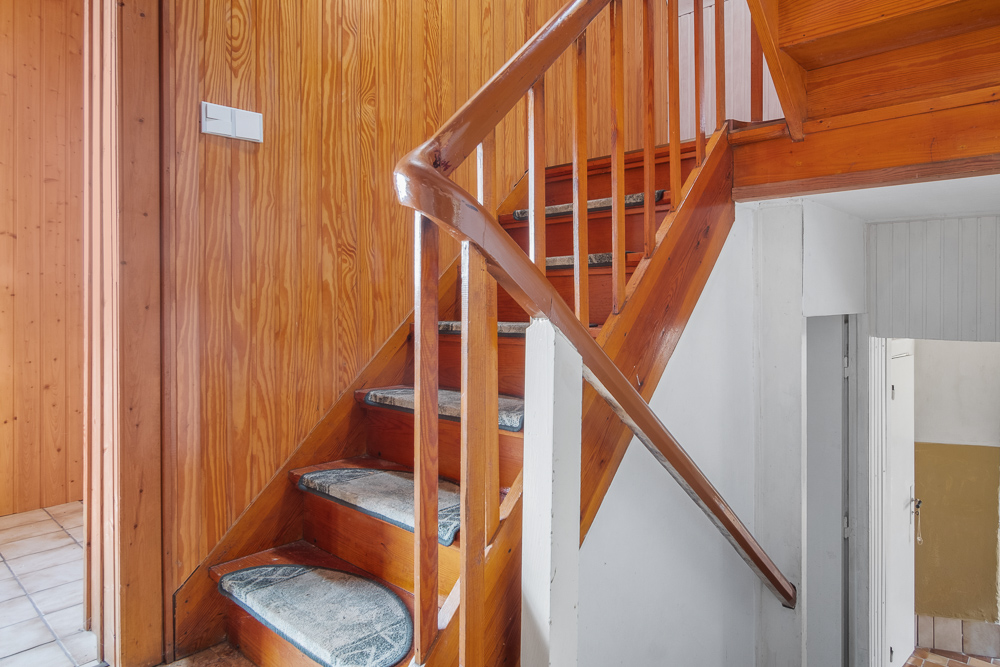 Holztreppe mit Teppichstufen in einem Flur mit vertäfelten Wänden.