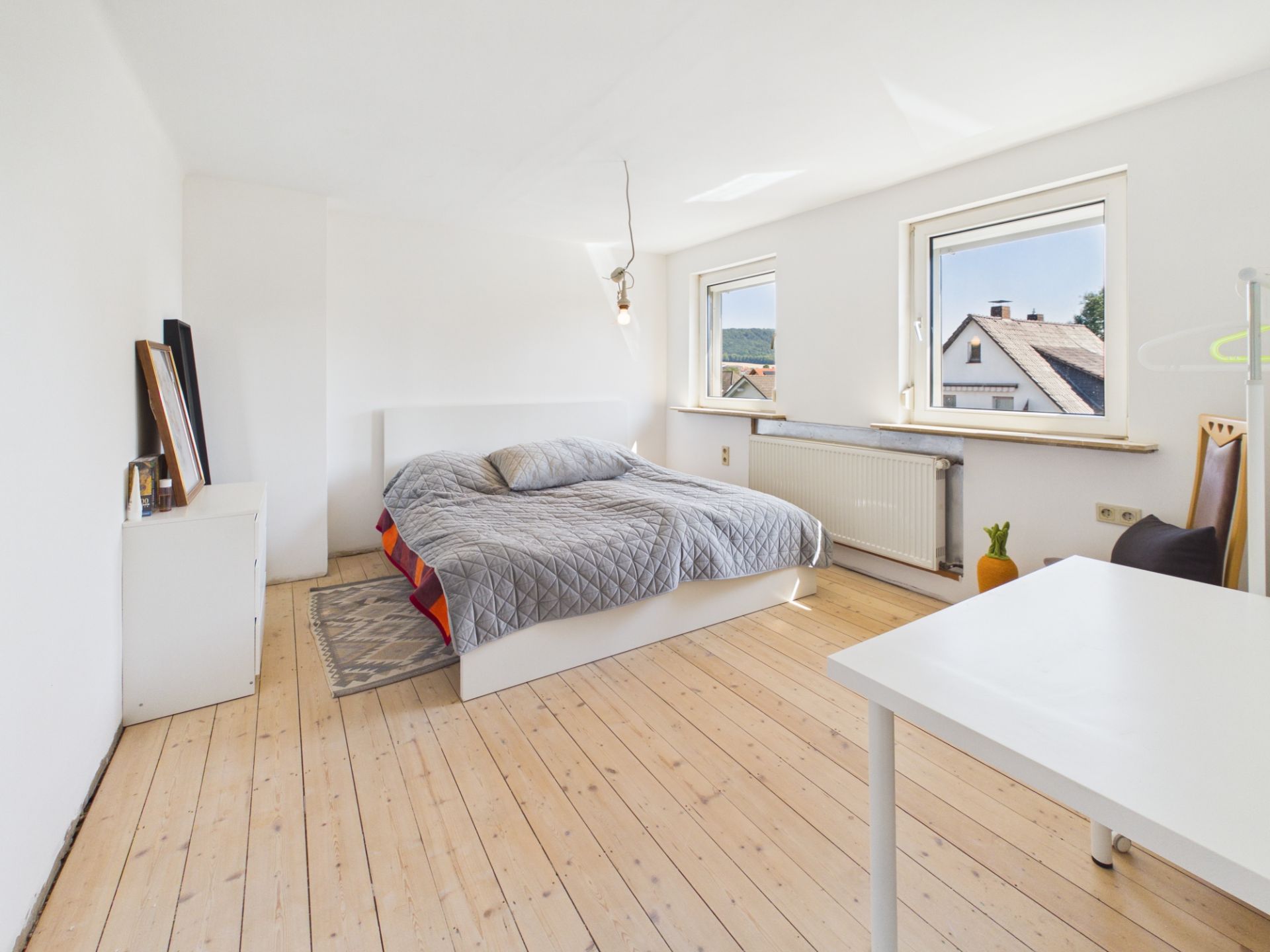 Helles Schlafzimmer mit Doppelbett, zwei Fenstern und Holzboden.