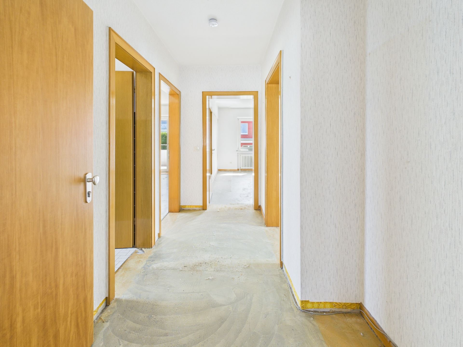 Heller Flur mit mehreren Holztüren in einer Wohnung, Boden teilweise unfertig.