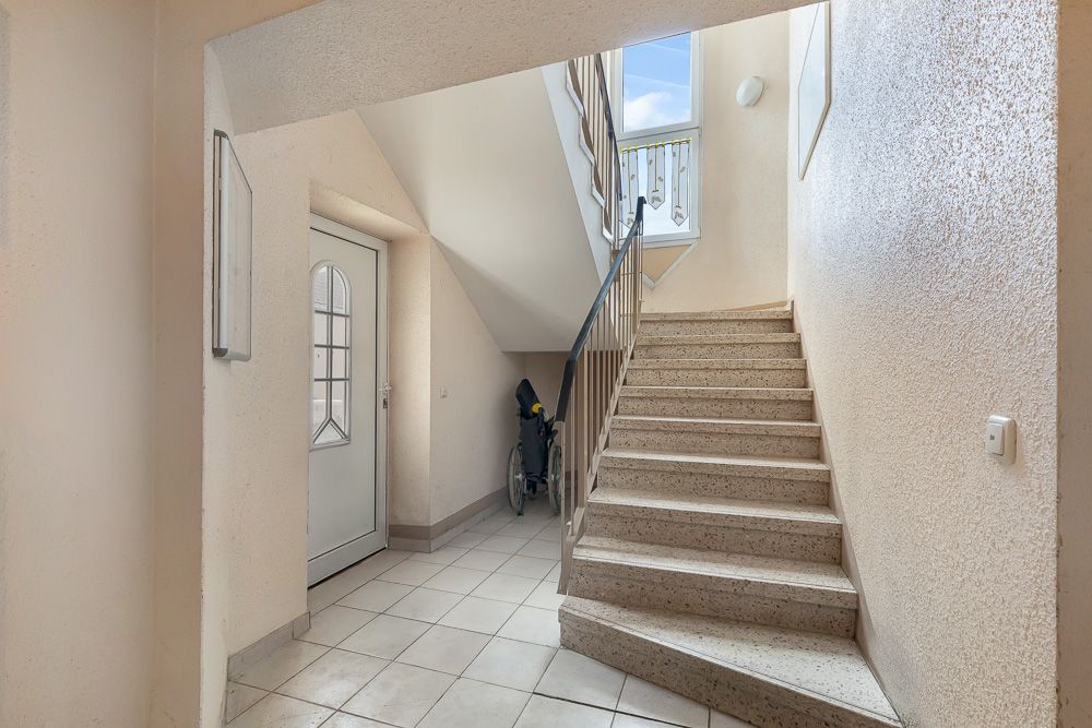 Heller Treppenhausflur mit weißer Tür, Aufgang und Fahrrad unter der Treppe.
