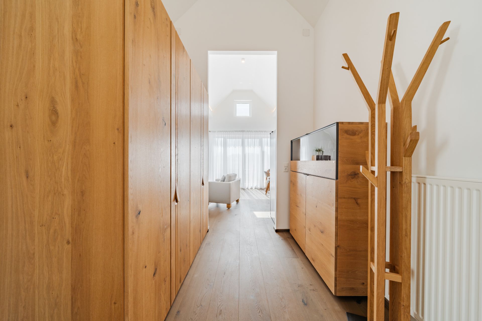 Heller Flur mit Holzmöbeln und Blick auf ein Wohnzimmer mit großen Fenstern.