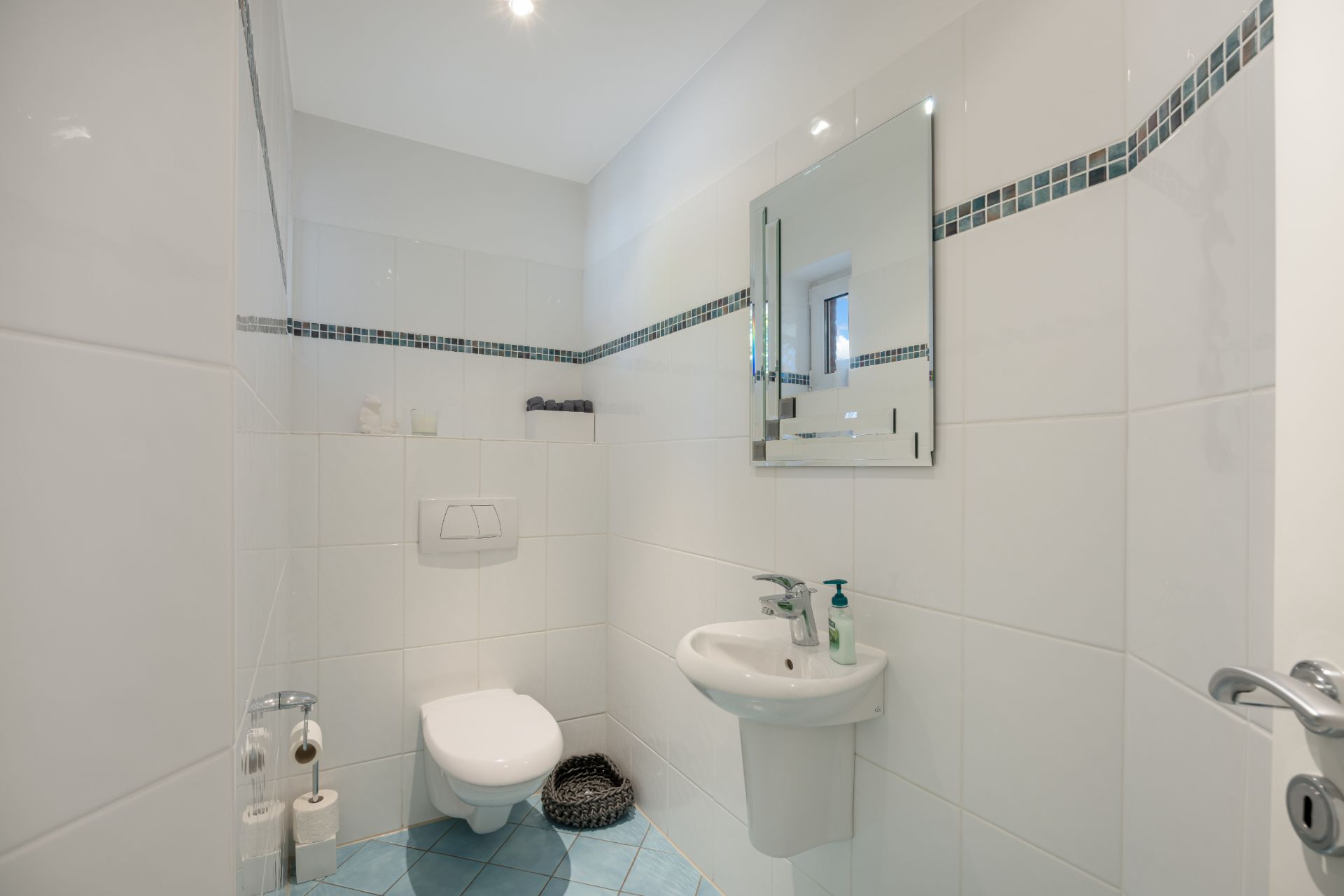 Kleines Bad mit WC, Waschbecken, Spiegel und weiß gefliesten Wänden.