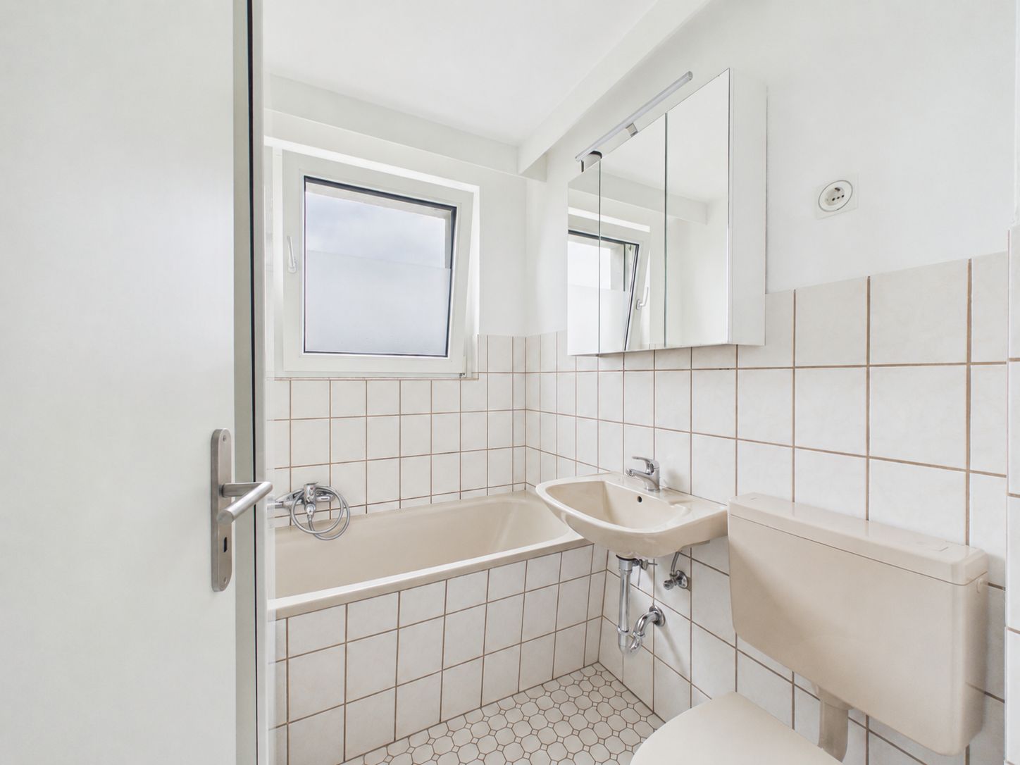 Helles Badezimmer mit Badewanne, Waschbecken und WC, gefliest und mit Fenster.