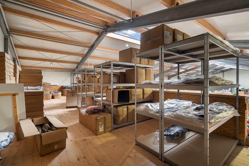 Dachbodenraum mit Holzfußboden, Regalen und vielen Kartons sowie gelagerten Gegenständen.