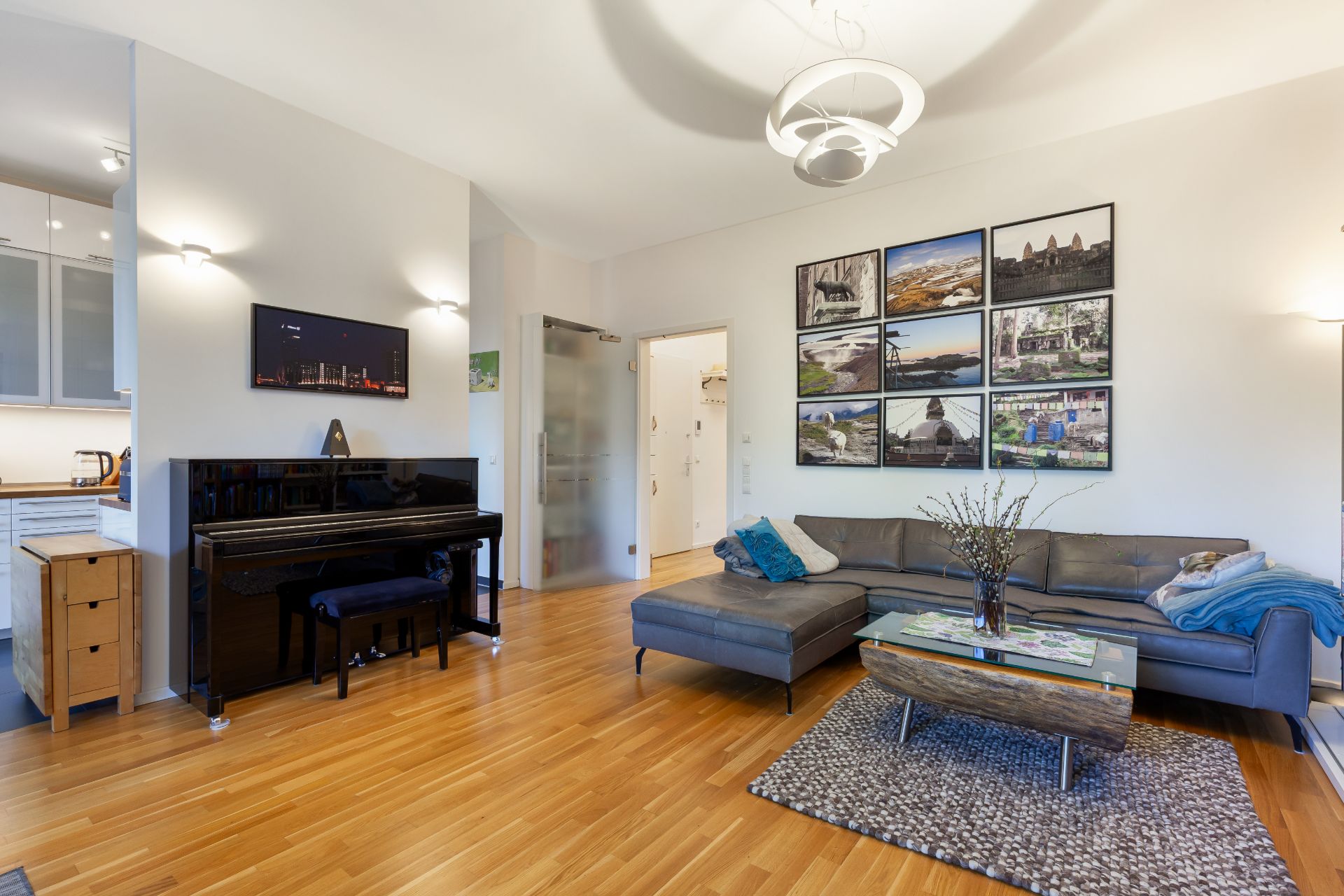 Helles Wohnzimmer mit Ecksofa, Couchtisch, Klavier und Bildern an der Wand.