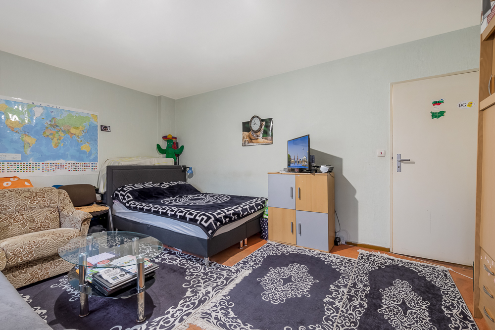Wohnzimmer mit Bett, Sofa, Teppichen, Glastisch und Schrank mit Fernseher.