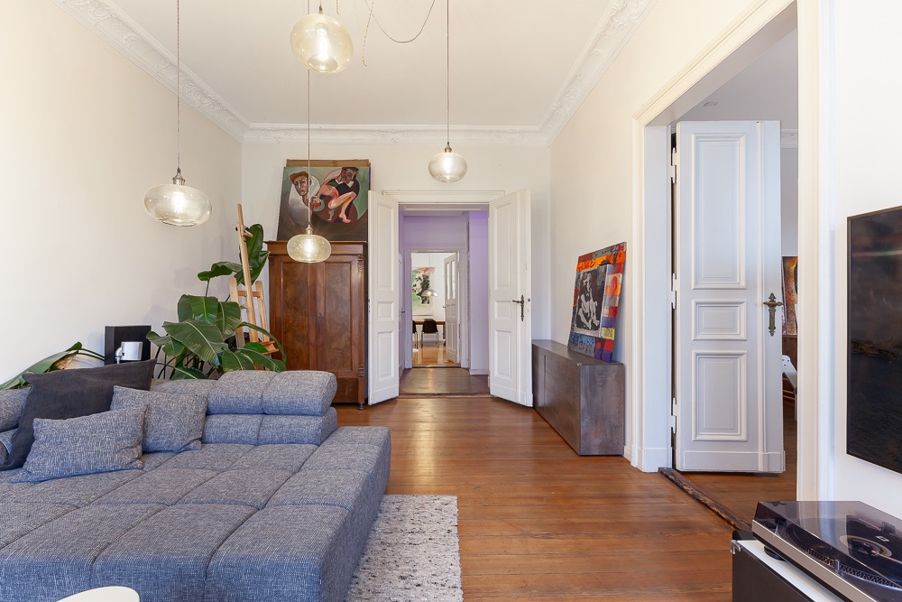 Modernes Wohnzimmer mit grauem Sofa, Holzboden, Pflanzen und Bildern an den Wänden.