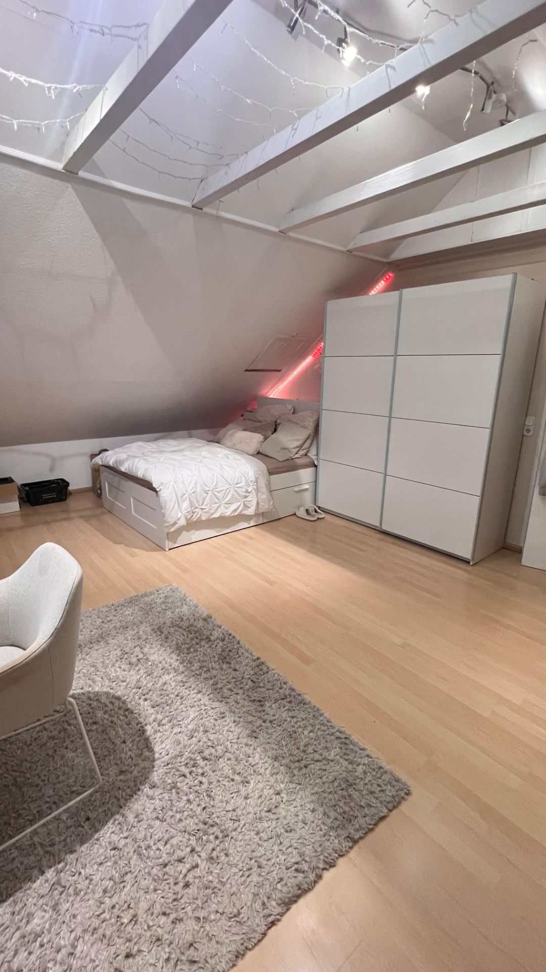 Helles Schlafzimmer mit Dachschräge, Bett, großem weißen Schrank und Teppich.