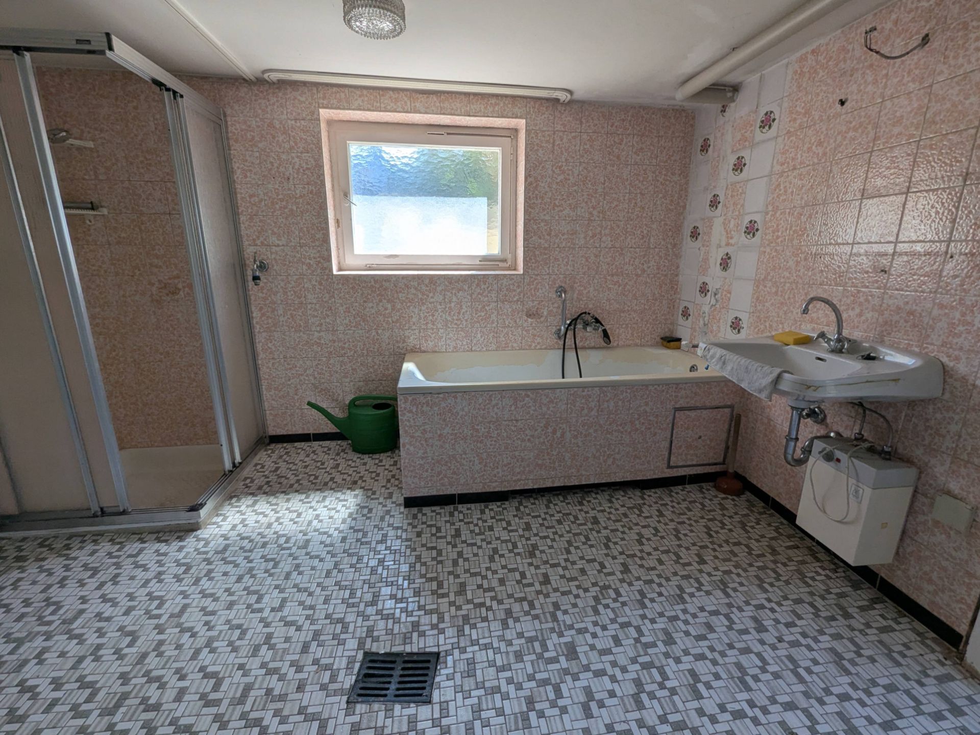Badezimmer mit Dusche, Badewanne, Waschbecken und kleinem Fenster, gefliester Boden.
