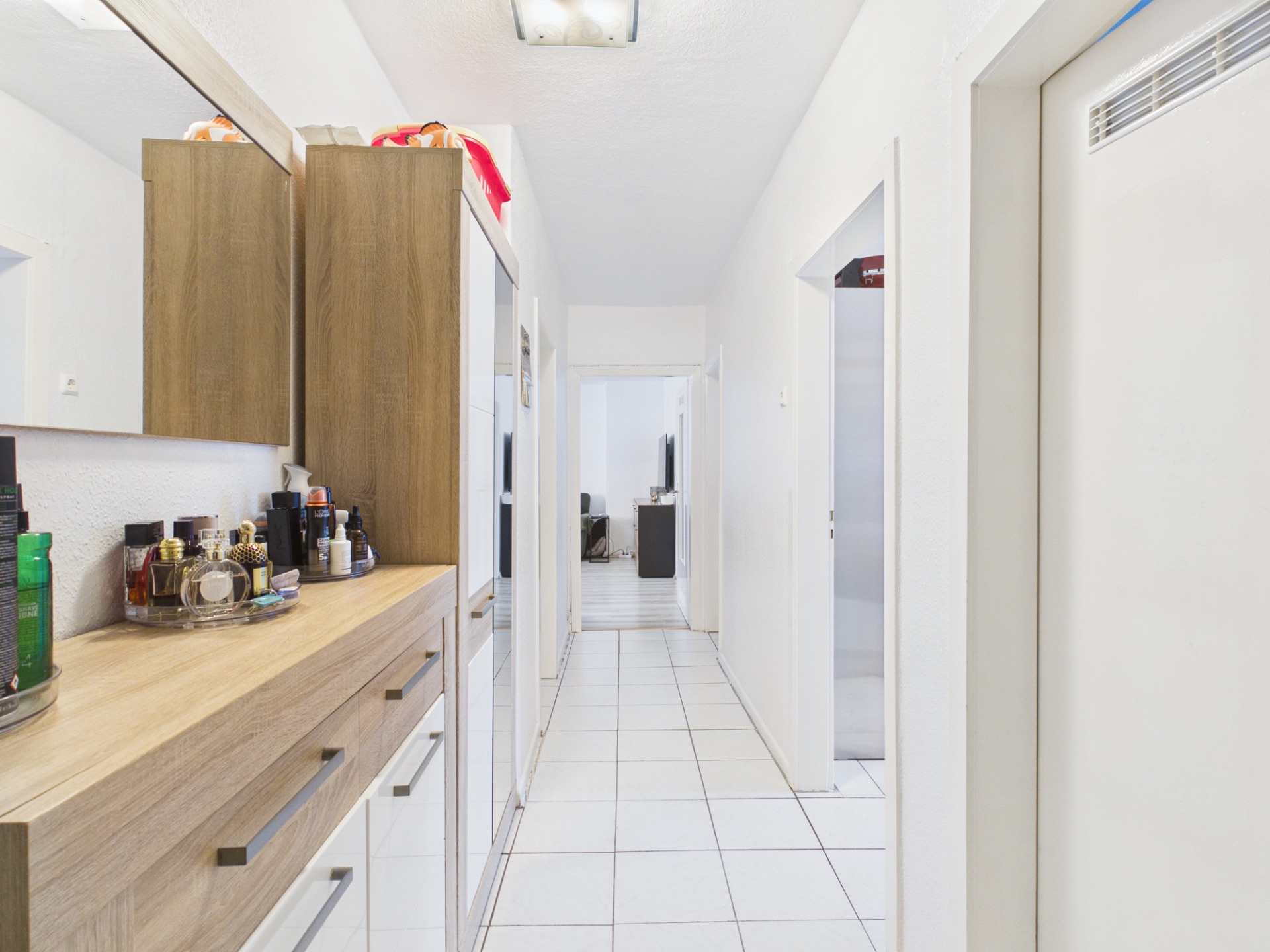 Heller Flur mit weißen Fliesen, Holzkommode und Wandspiegel in einer Wohnung.