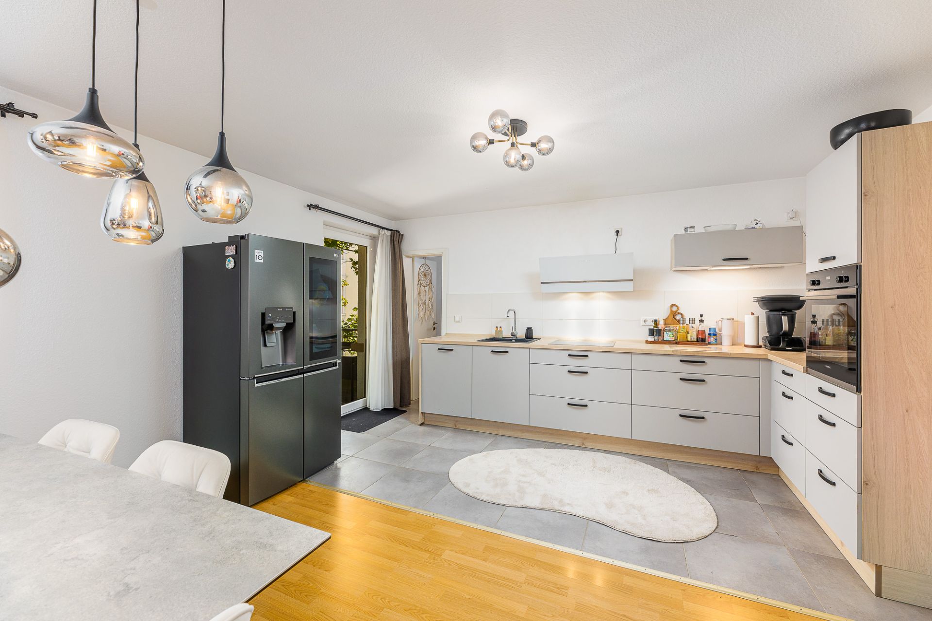 Helle moderne Küche mit Esstisch, Hängelampen und großem Kühlschrank.