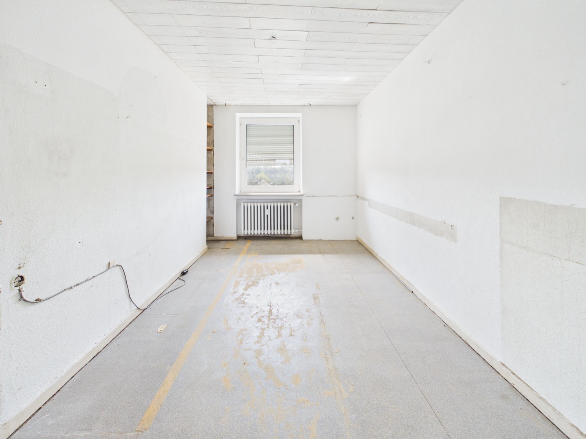 Leerer Raum mit weißen Wänden, Fenster und Heizkörper am Ende des Zimmers.