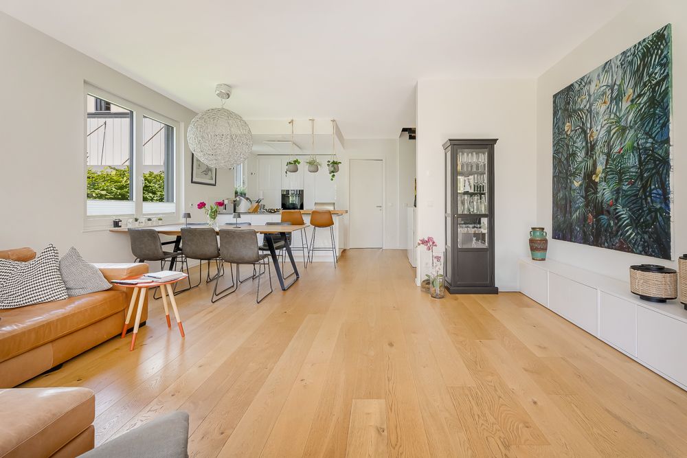 Modernes Wohnzimmer mit Holzboden, Ledersofa, Esstisch und großer Wandkunst.