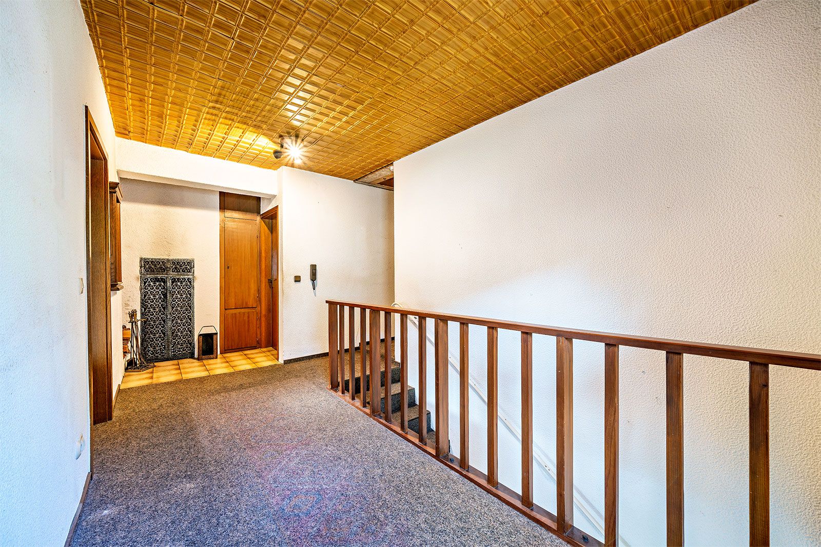 Flur mit Holzgittertreppe, Teppichboden und gelbem Holzdecken, Türen zu weiteren Räumen.
