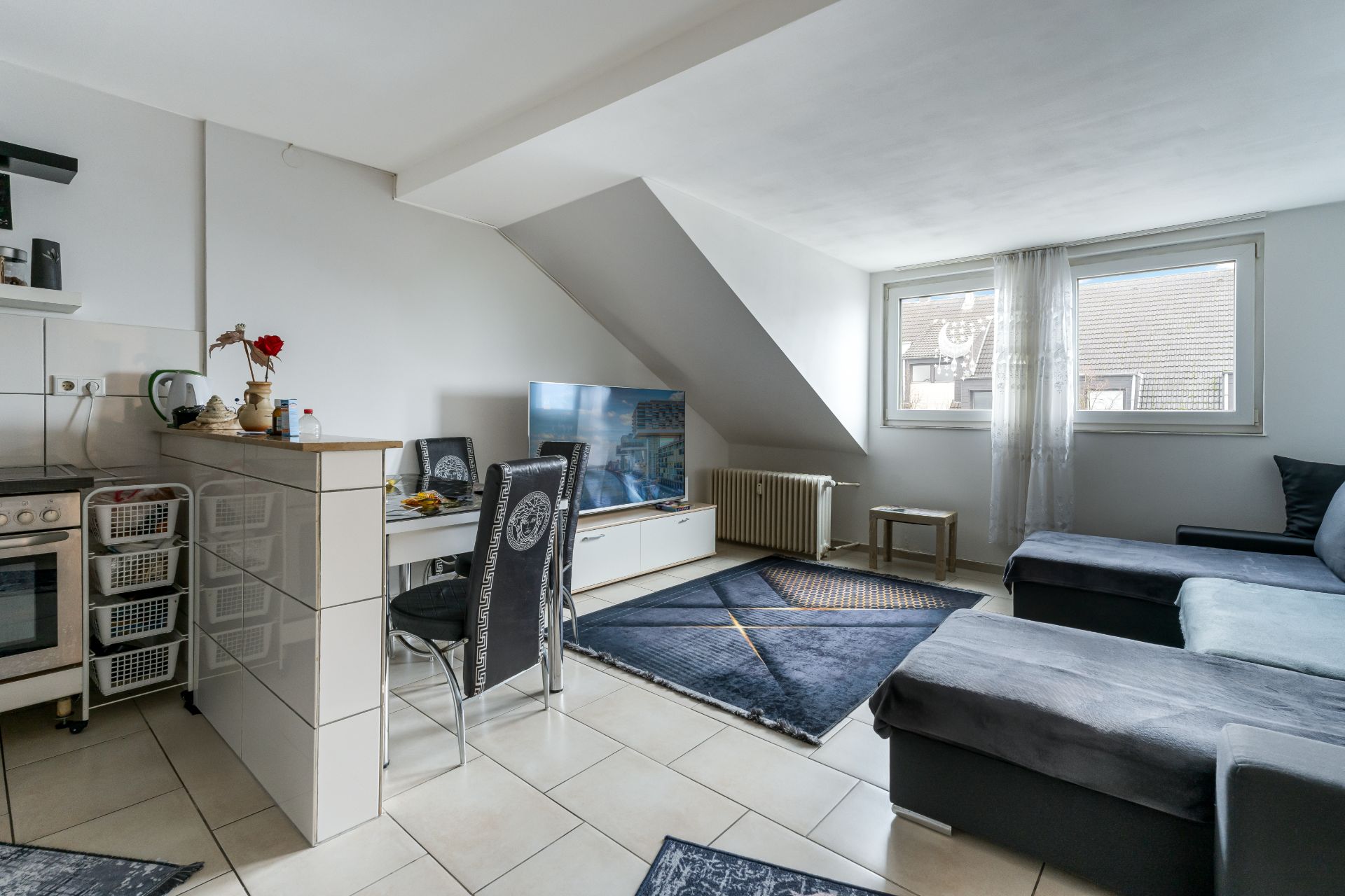 Wohnzimmer mit Ecksofa, Fernseher, Esstisch und Küchenbereich unter Dachschräge.