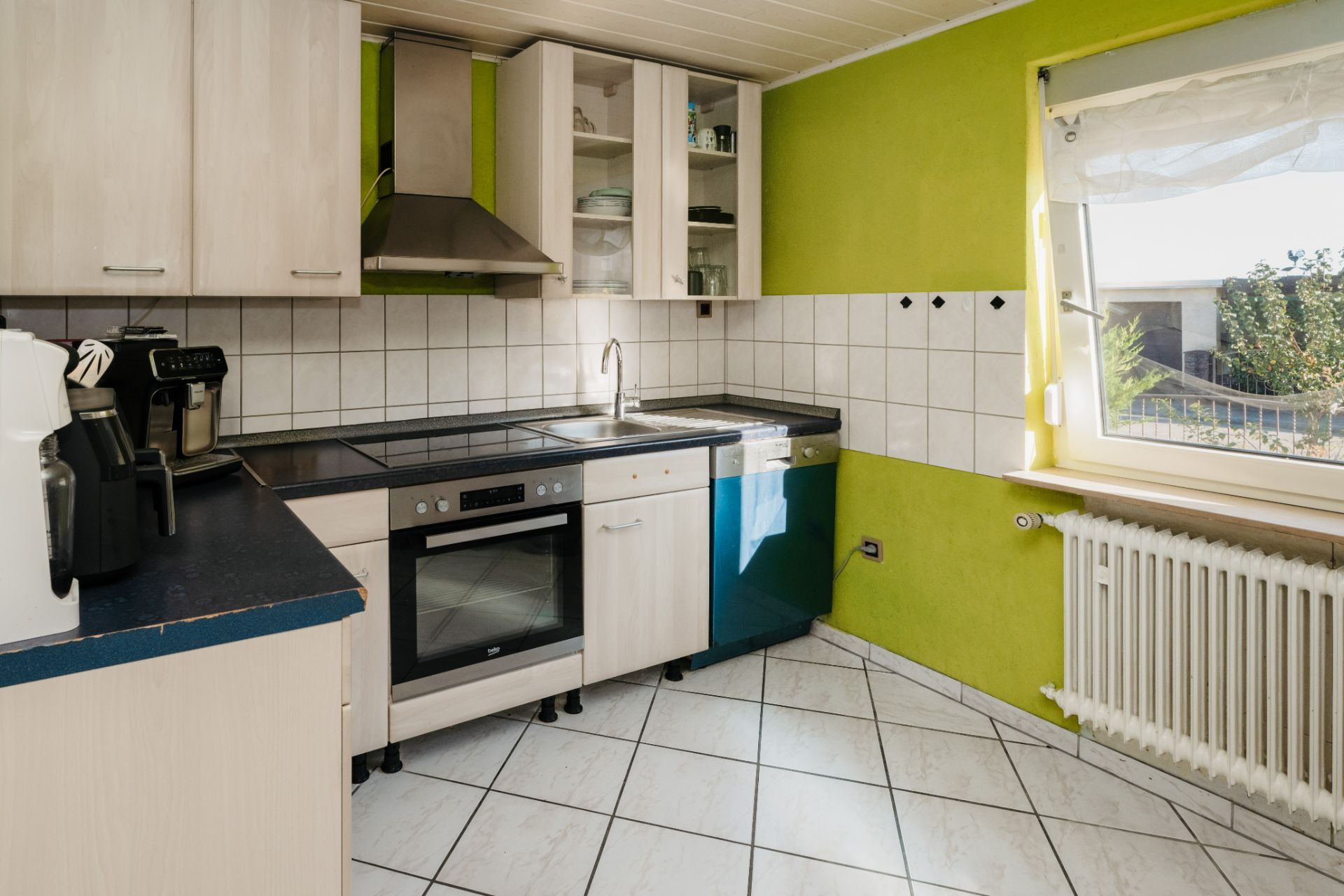 Helle Küche mit weißen Schränken, Elektrogeräten und einem Fenster mit Blick nach draußen.