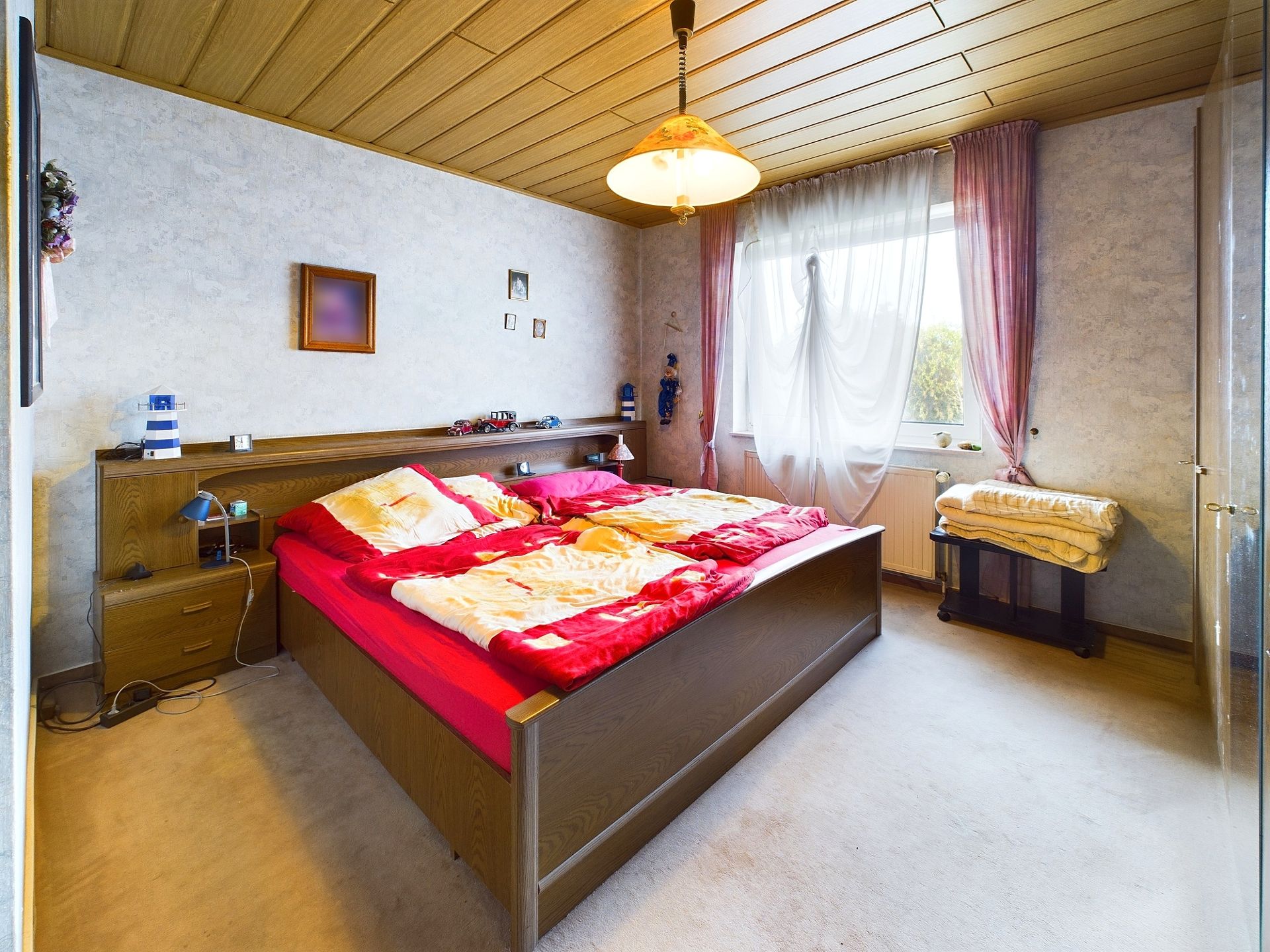 Schlafzimmer mit großem Bett, Nachttischlampen, Fenster mit Vorhängen und Decken auf einer Bank.
