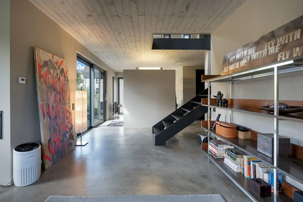 Moderner Wohnbereich mit Regal, Kunstwerk, Treppe und großen Fenstern.