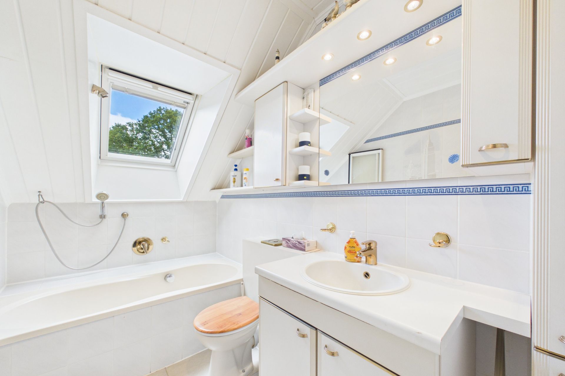 Helles Badezimmer mit Badewanne, Waschbecken, Spiegel, WC und Dachfenster.