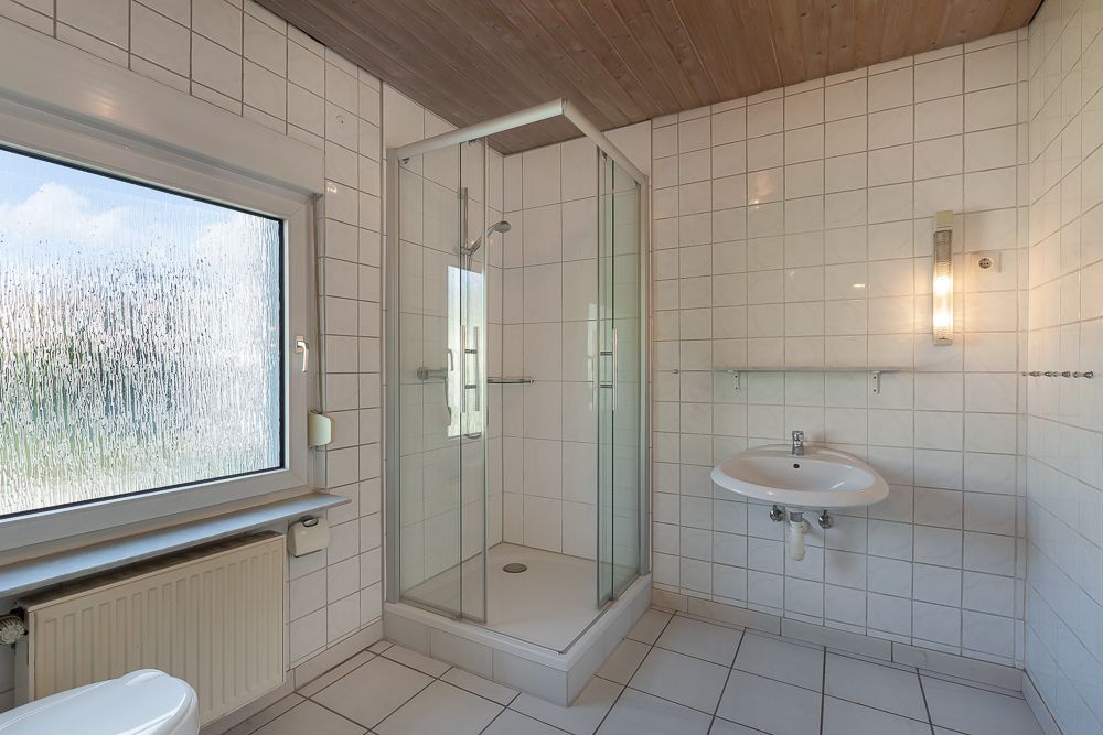 Helles Badezimmer mit Dusche, großem Fenster, Waschbecken und Wandfliesen.