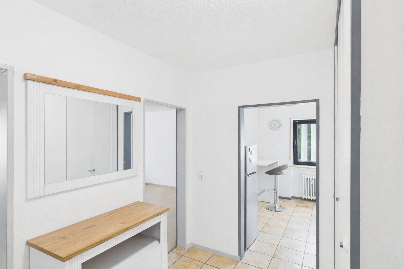 Heller Flur mit Spiegel, Kommode, Blick in Küche mit Barhocker und Fenster.
