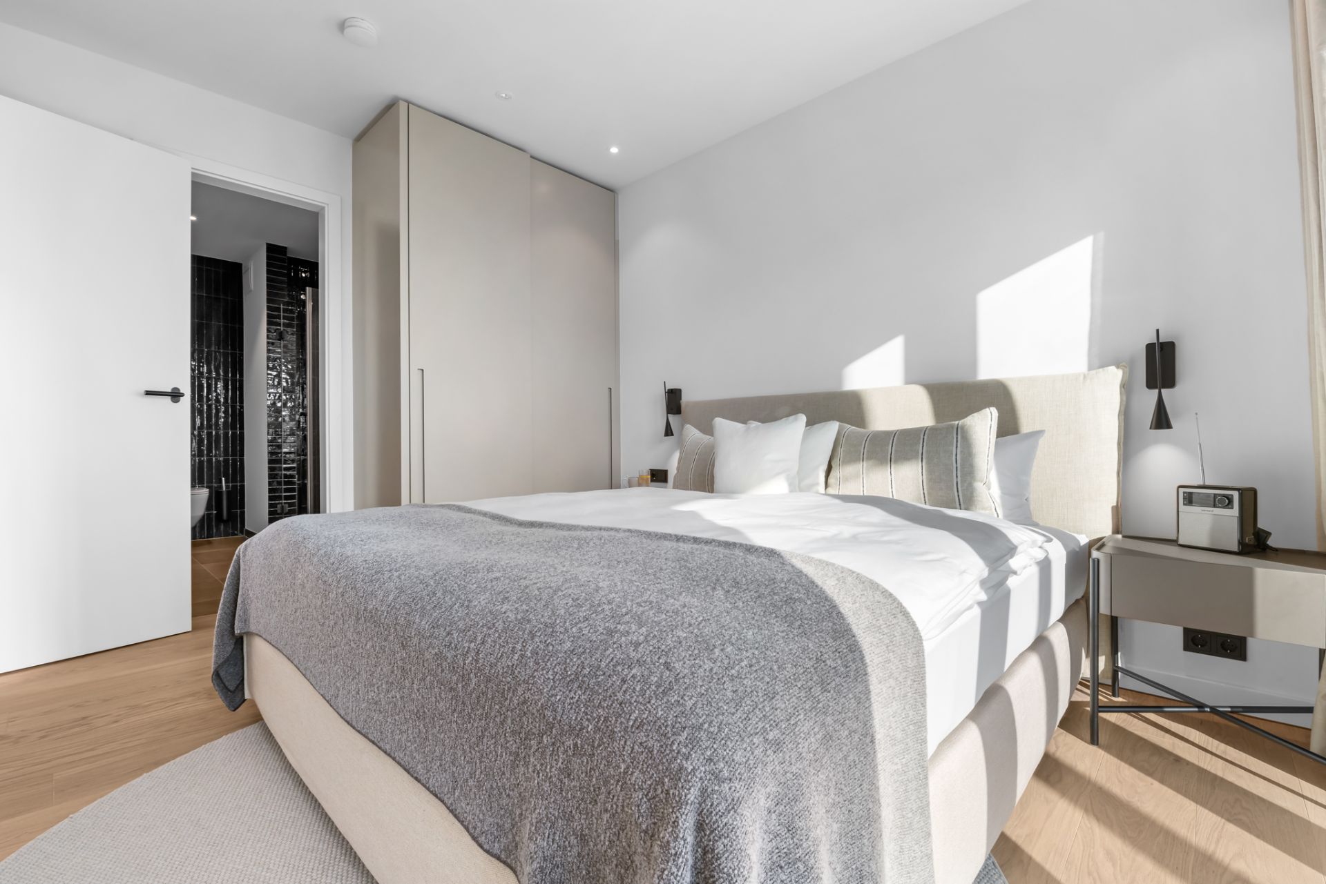 Helles Schlafzimmer mit großem Bett, Nachttisch, Kleiderschrank und offen stehender Tür.