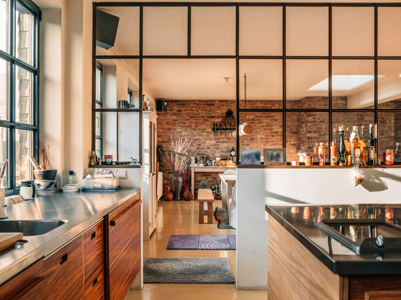 Moderne Küche mit Holzschränken, Glaswand und Blick ins Wohnzimmer mit Ziegelwand.