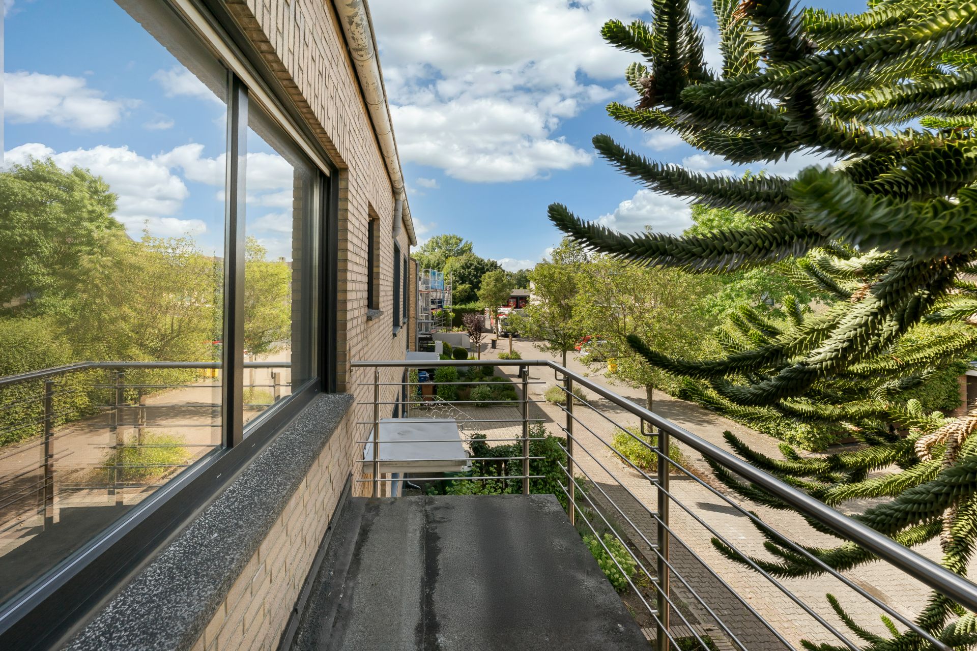 Schmaler Balkon mit Metallgeländer an einem Wohnhaus, Blick auf Straße und Bäume.