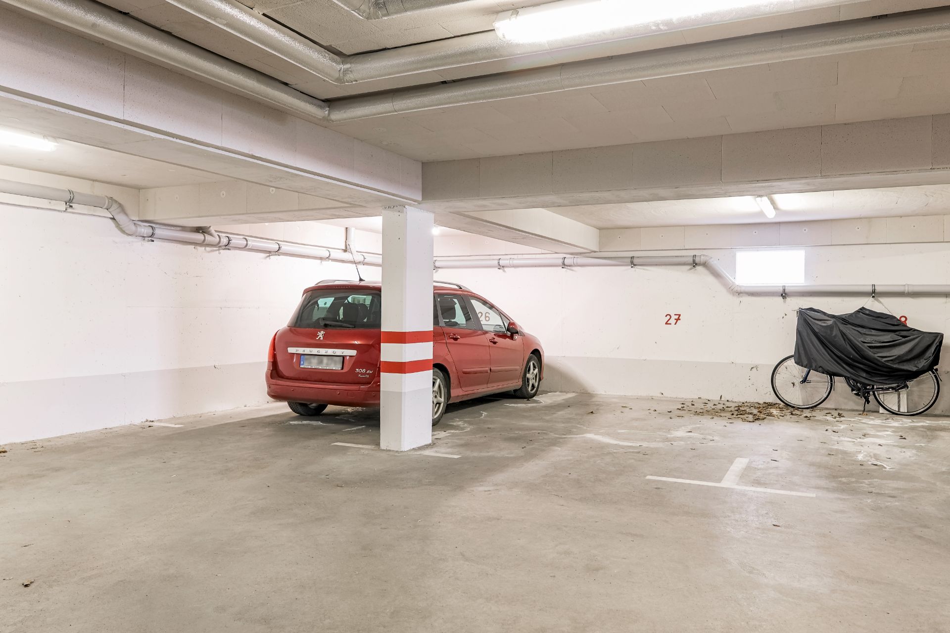 Tiefgaragenstellplatz mit rotem Auto und abgedecktem Fahrrad an der Wand.