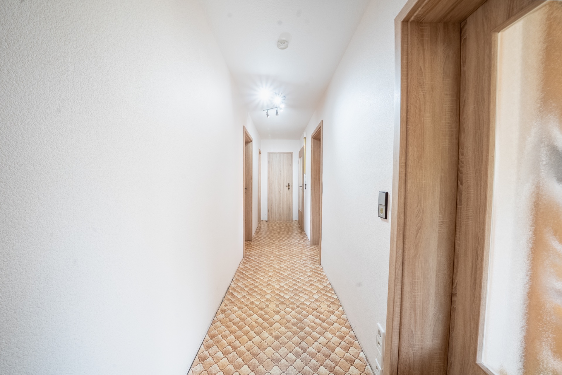 Heller Flur mit Fliesenboden und mehreren Holztüren auf beiden Seiten.